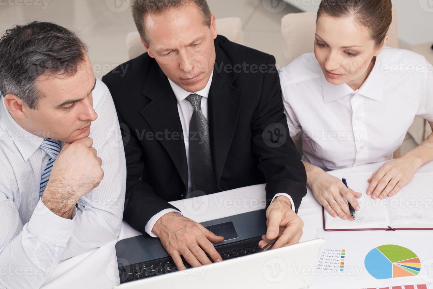 Business people at work. Top view of three cheerful business people in formalwear sitting at the table and looking at the laptop photo