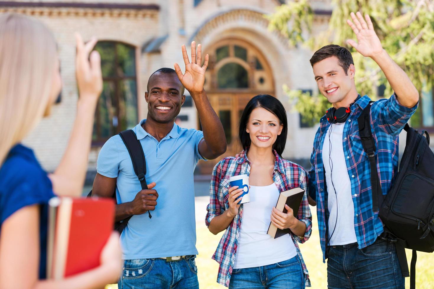 Saying hi to friends. Rear view of young woman holding books and waving to her friends standing outdoors photo