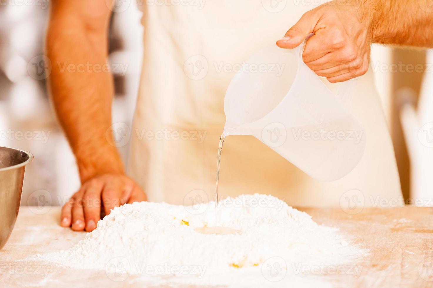 Adding some water to flour. Close-up of male baker pouring water on the flour photo