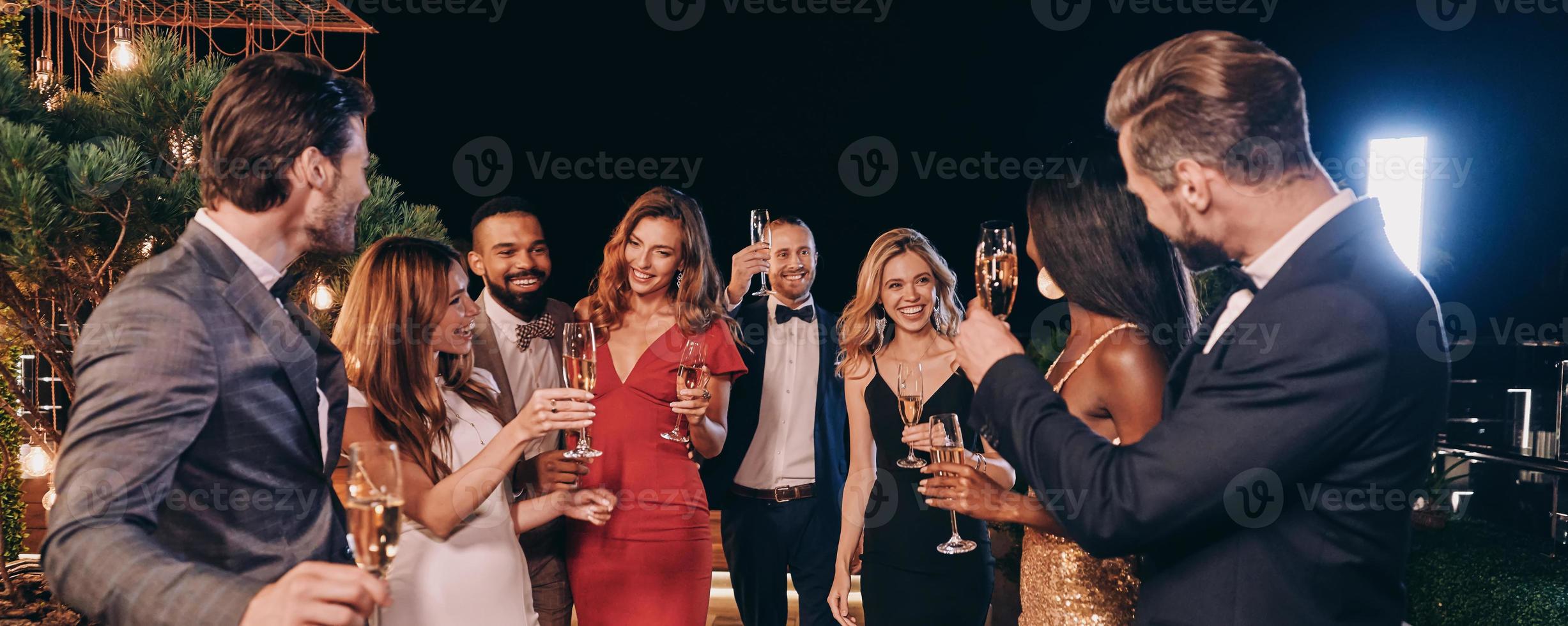 grupo de personas hermosas en ropa formal comunicándose y sonriendo mientras pasan tiempo en una fiesta de lujo foto