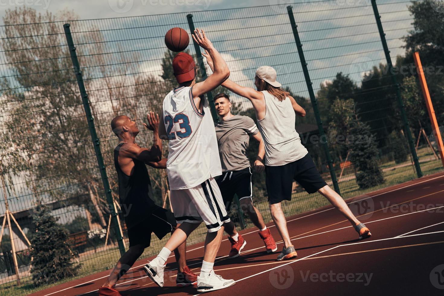 Training to become the best. Group of young men in sports clothing playing basketball while spending time outdoors photo