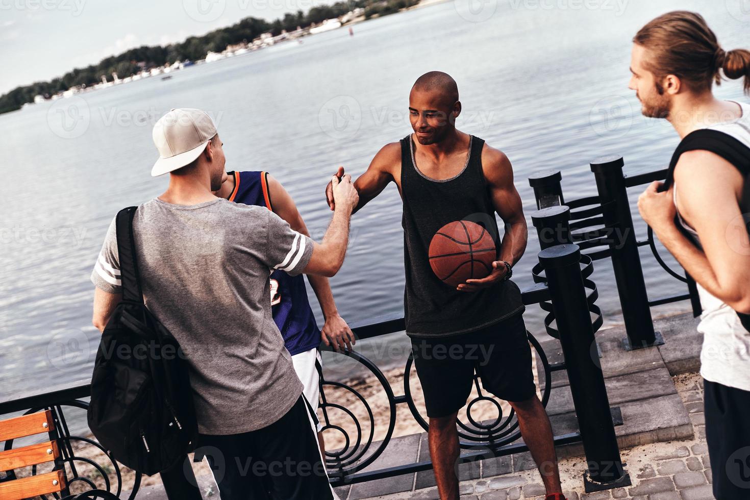 See you soon. Two young men in sports clothing shaking hands while standing among friends outdoors photo