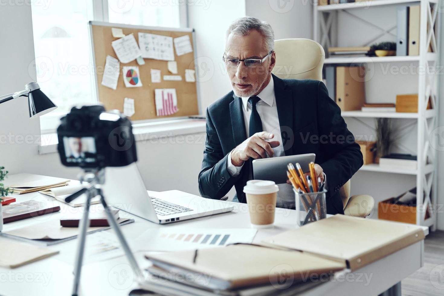Senior man in elegant business suit using digital tablet while making social media video photo
