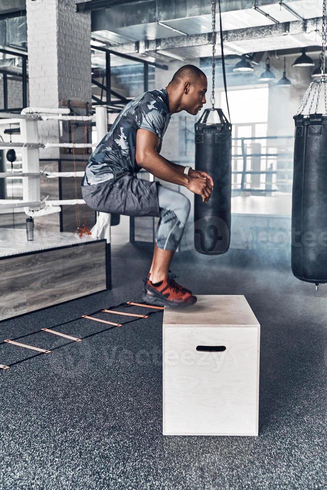 Doing his best. Handsome young African man in sport clothing jumping while exercising in the gym photo