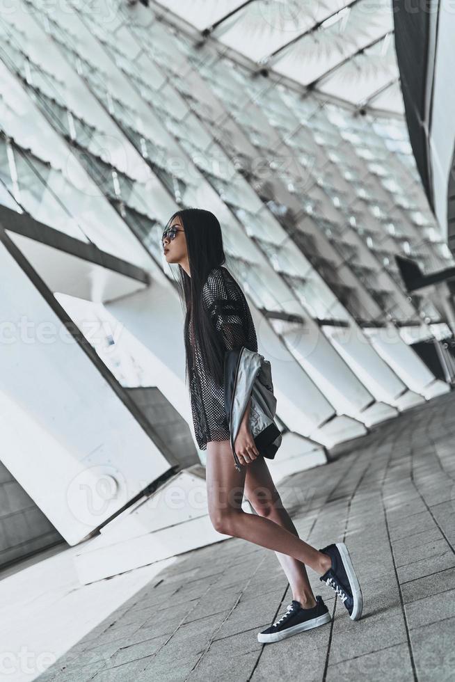 segura de su estilo. toda la longitud de una hermosa joven con ropa informal mirando hacia otro lado mientras está de pie al aire libre foto