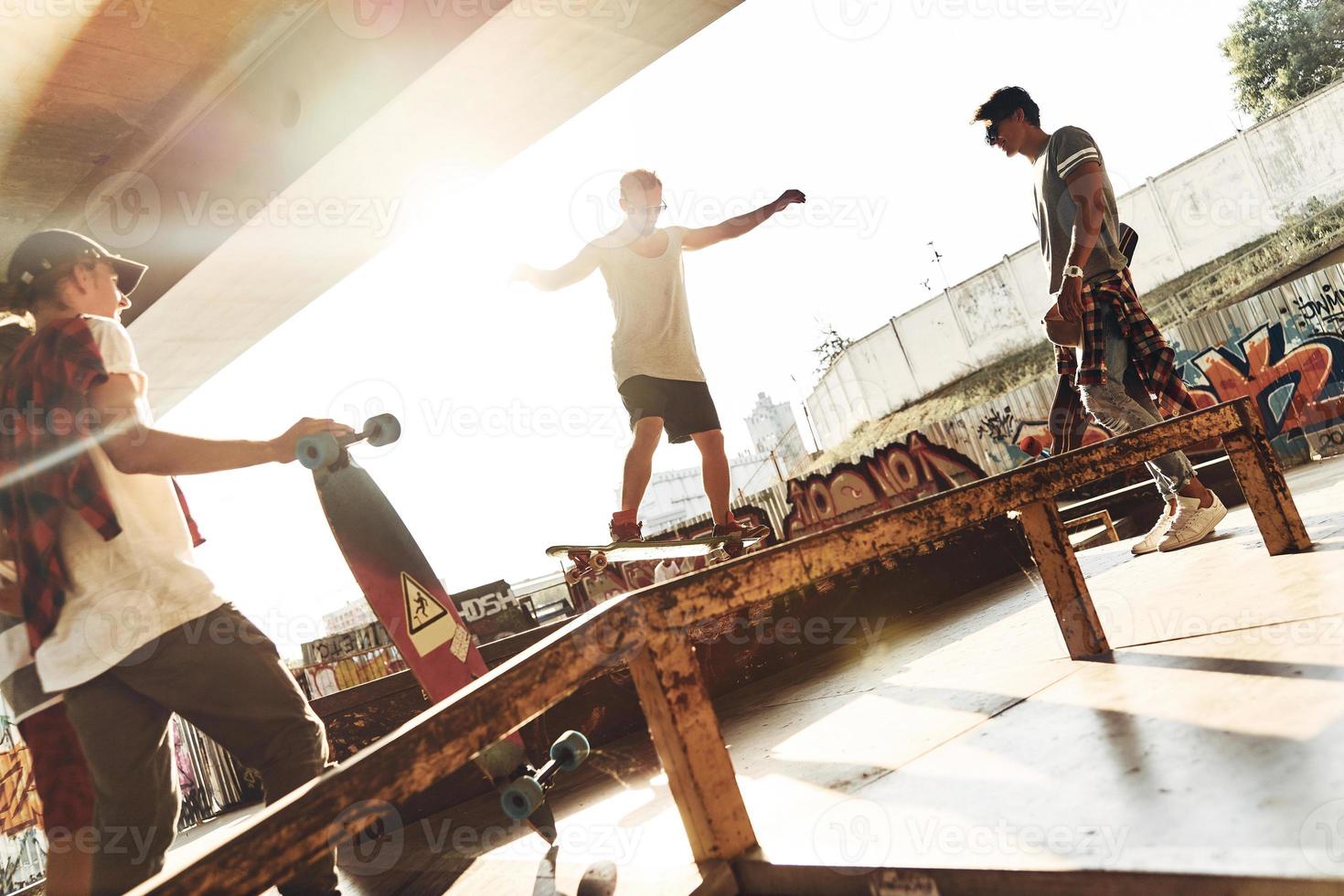 Challenging themselves. Group of young people skateboarding while hanging out at the skate park outdoors photo