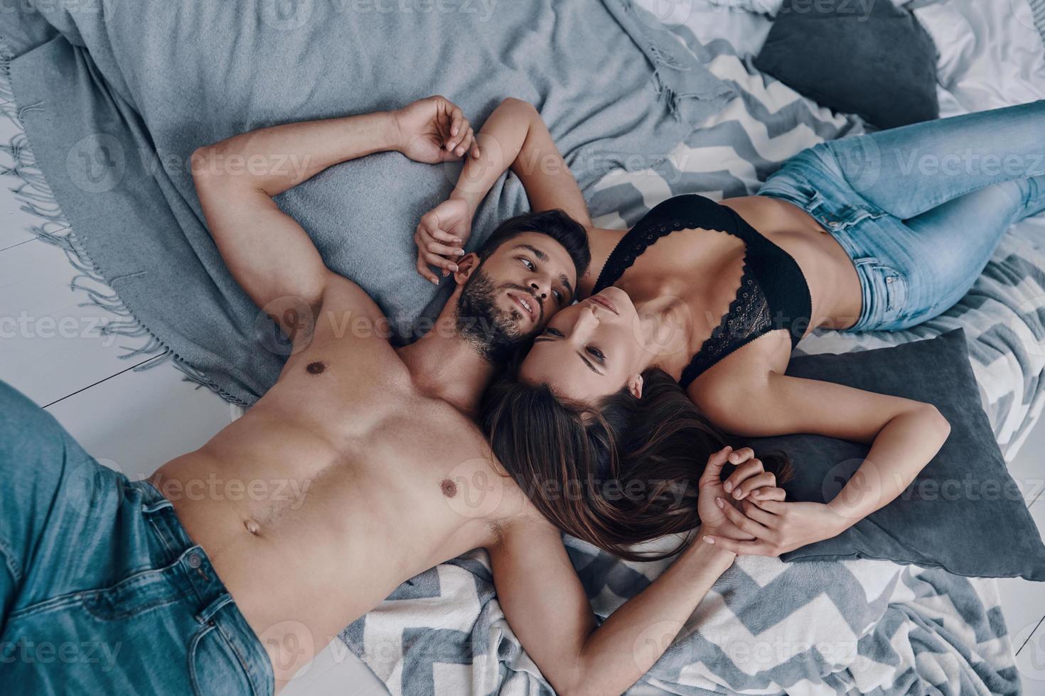 momentos de intimidad. vista superior de una hermosa pareja joven semi-vestida acostada cara a cara mientras pasa tiempo en el dormitorio foto