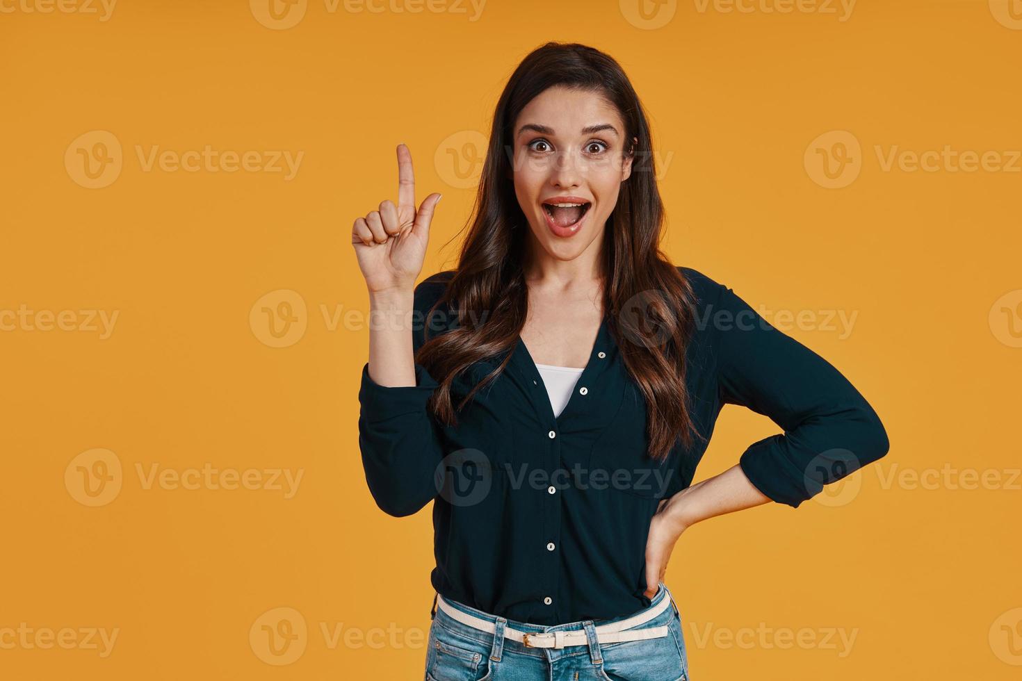 Attractive young woman in casual clothing gesturing and smiling while standing against yellow background photo