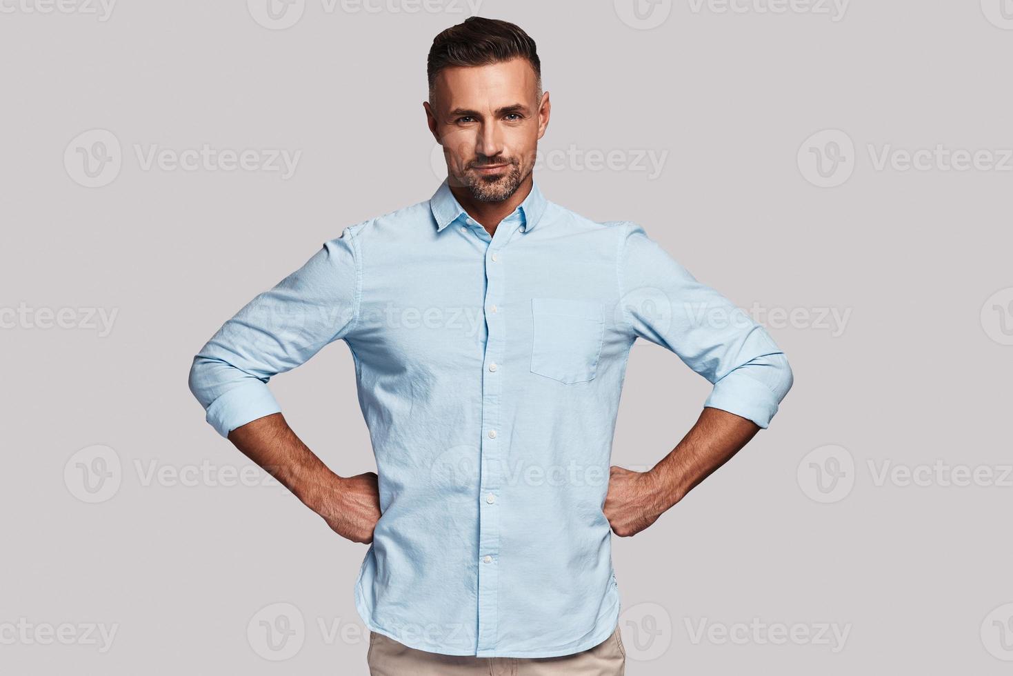 Taking everything seriously. Handsome young man smiling and looking at camera while standing against grey background photo