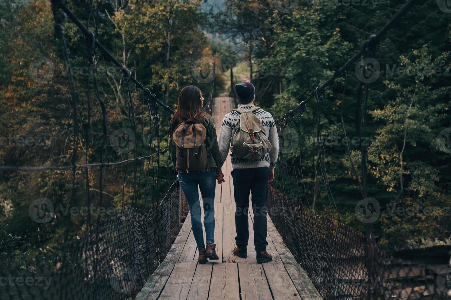 Exploring the world together. Full length rear view of young couple holding hands while walking on the suspension bridge photo