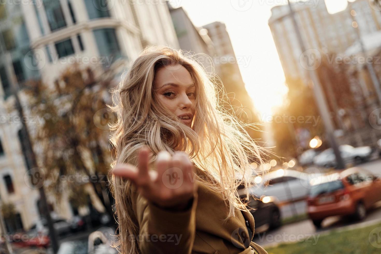 chica irresistible. atractiva joven mujer sonriente mirando a la cámara y gesticulando mientras está de pie al aire libre foto