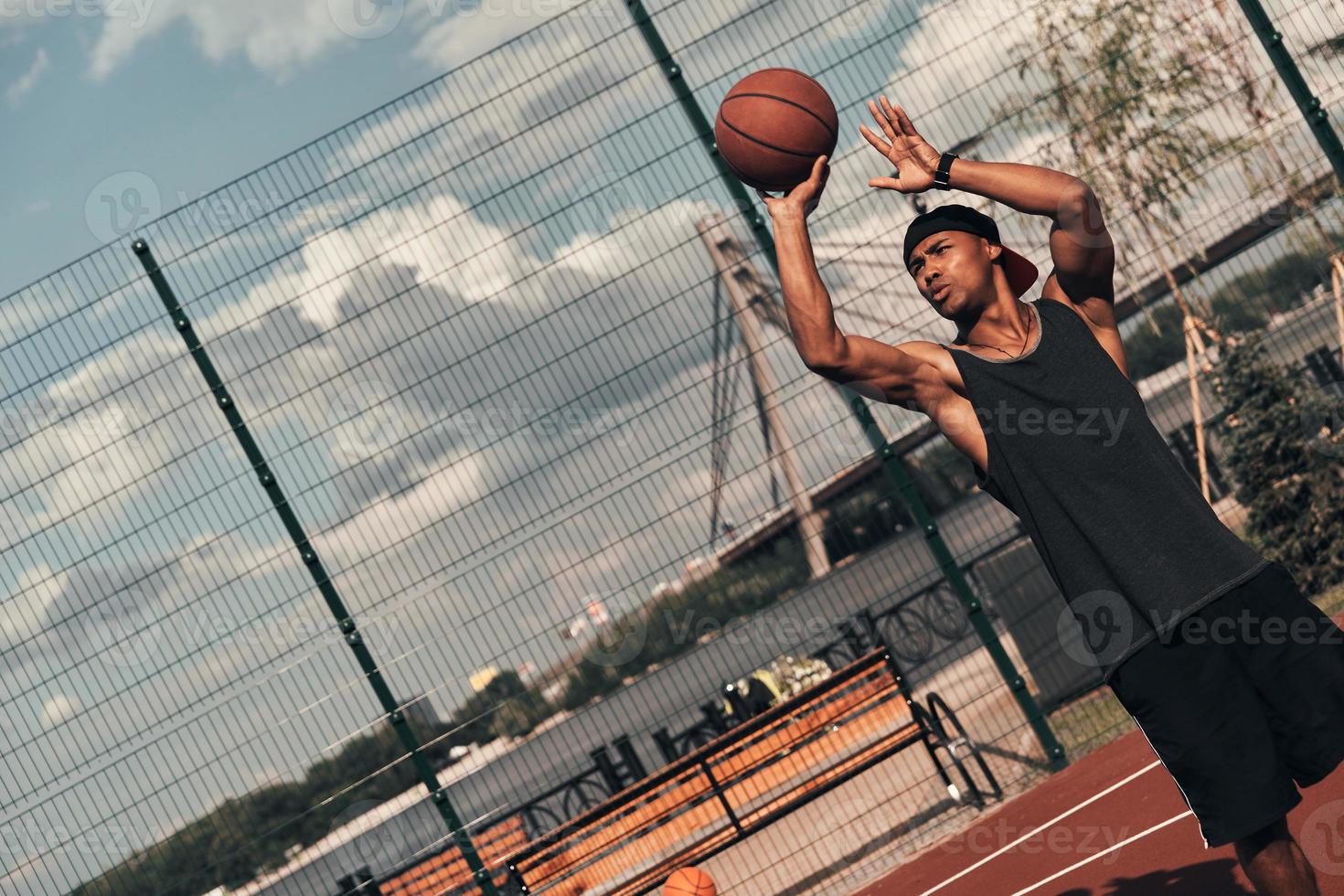 Careful shooting. Young African man in sports clothing throwing a ball while playing basketball outdoors photo