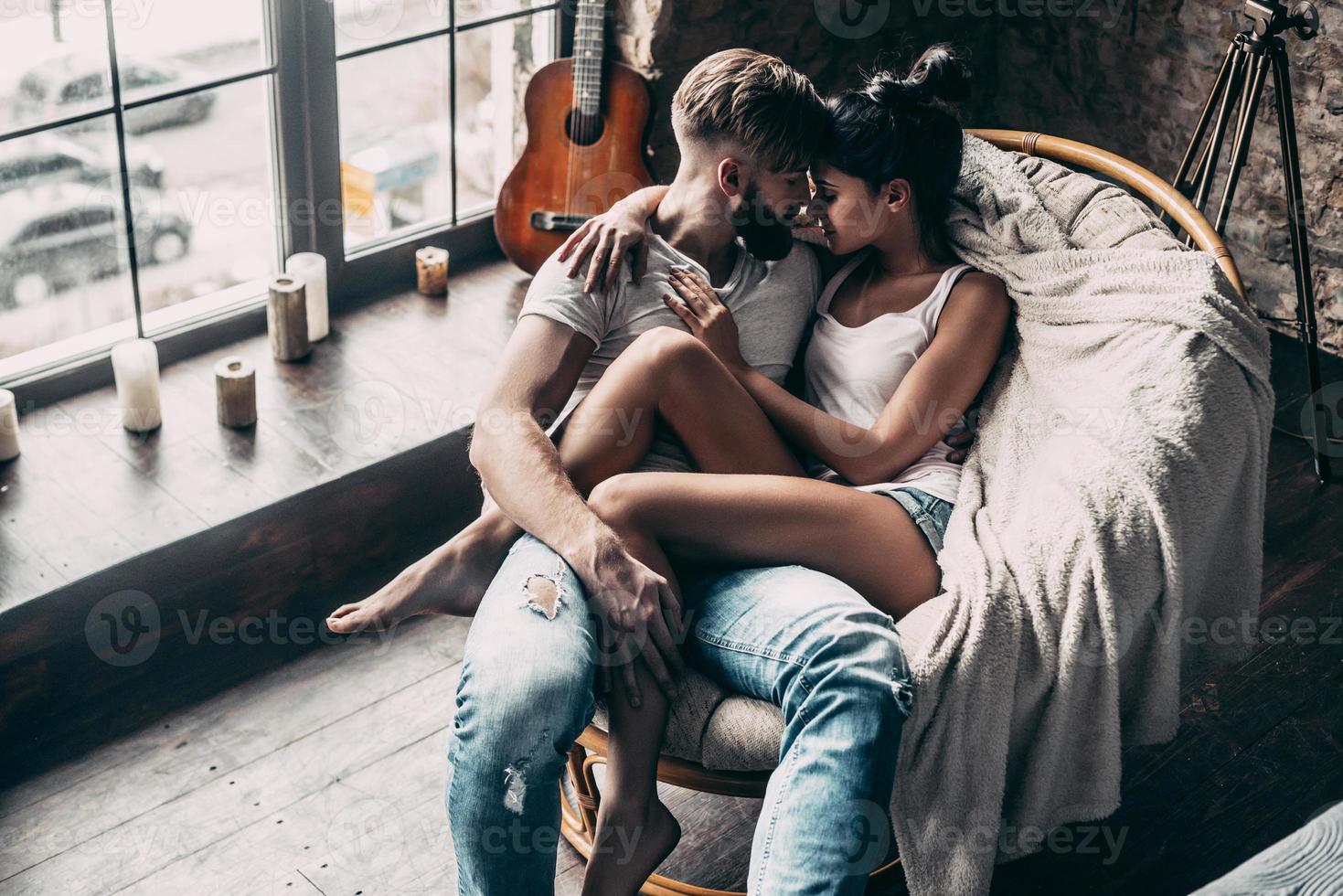 One and only. Top view of beautiful young couple embracing while sitting face to face in a big chair at home photo