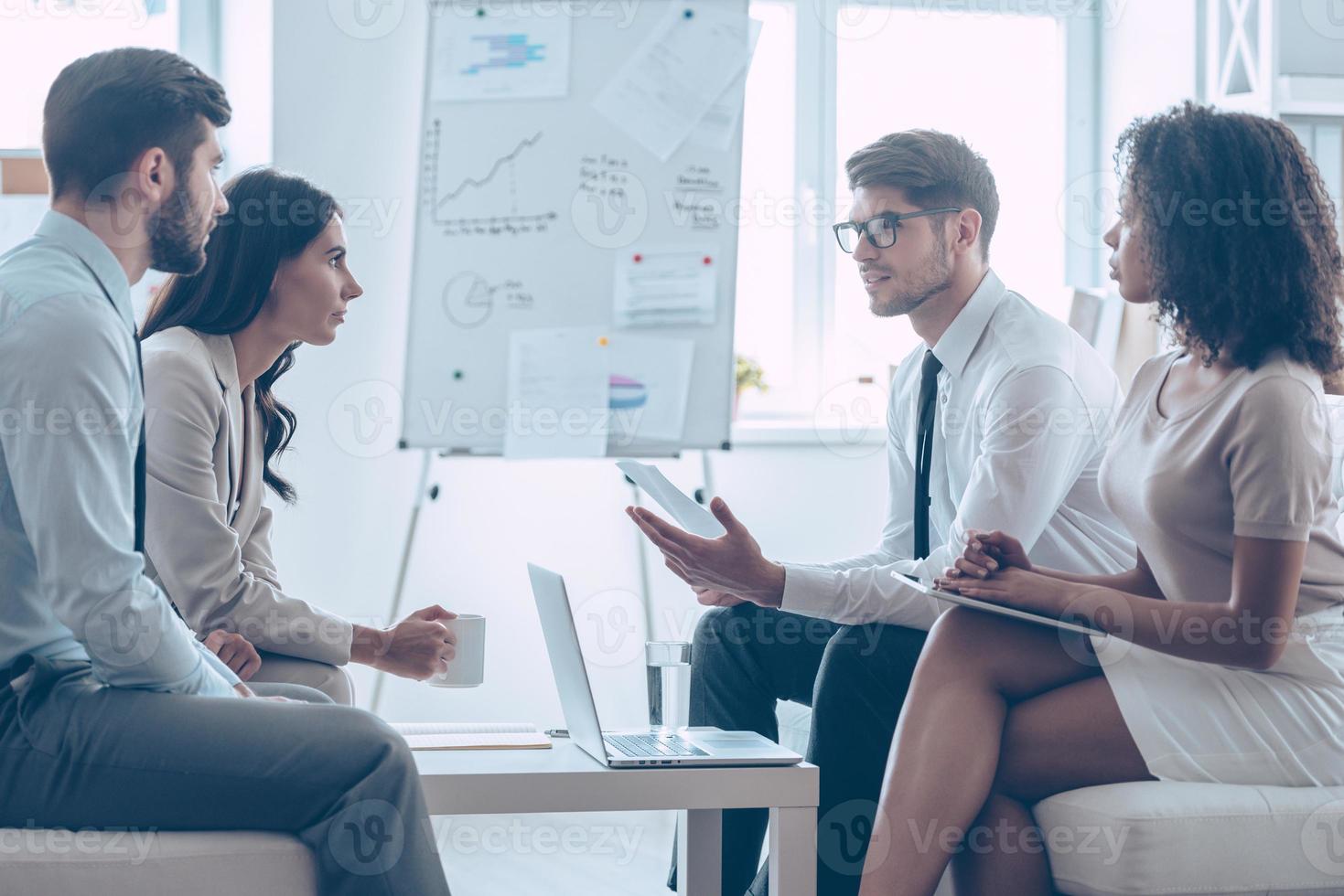 Presenting new business strategy. Young handsome man gesturing and discussing something with his coworkers while sitting on the couch at office photo