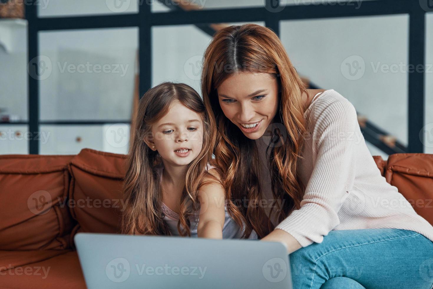 Young beautiful mother and her little daughter bonding together and smiling while using laptop at home photo