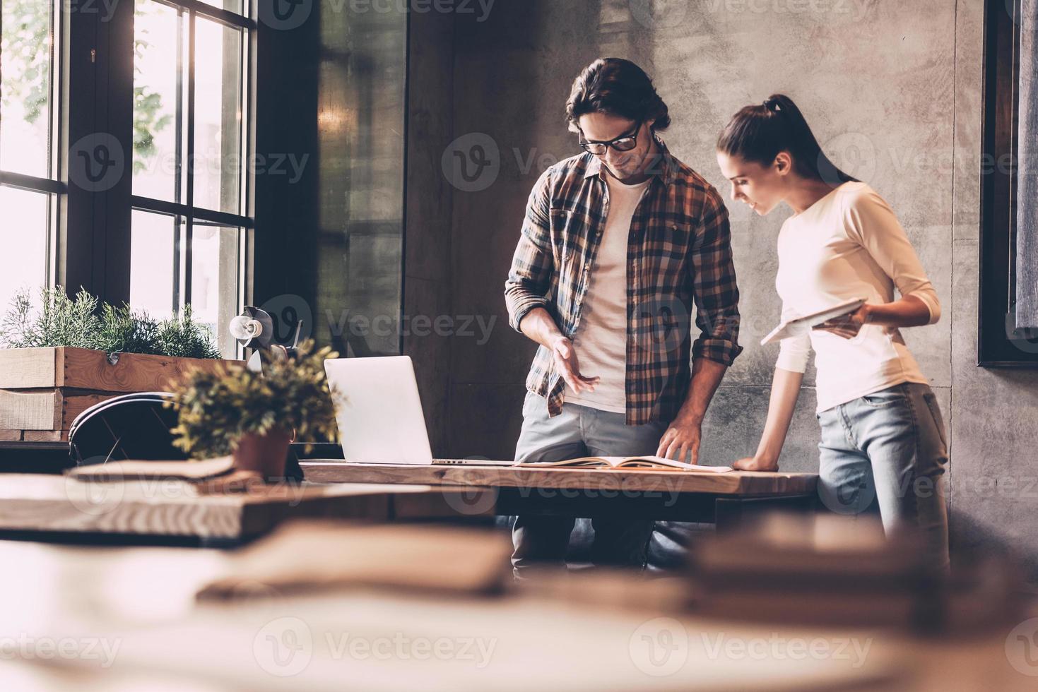 discutiendo negocios con un colega. un joven y una mujer confiados trabajando juntos mientras están cerca del escritorio en una oficina creativa foto