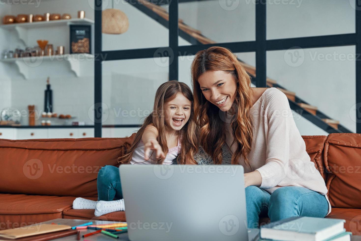 Young beautiful mother and her little daughter bonding together and smiling while using laptop at home photo
