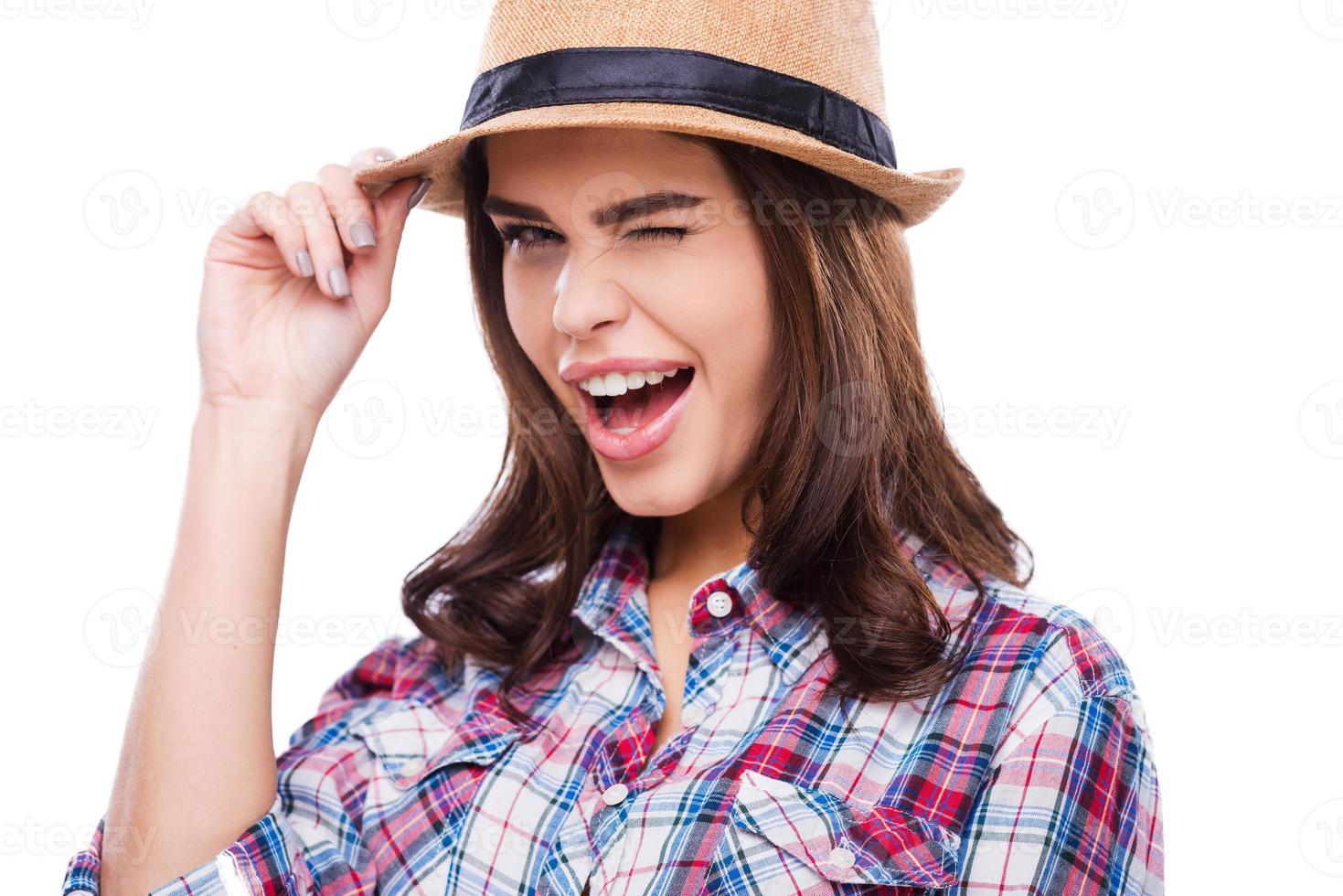 Winking beauty. Beautiful young woman in funky wear adjusting hat and winking at camera while standing against white background photo