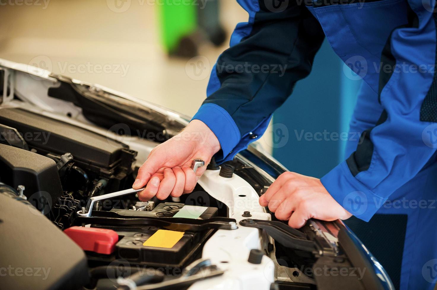 Mechanic at work. Close-up of man in uniform repairing car while standing in workshop photo
