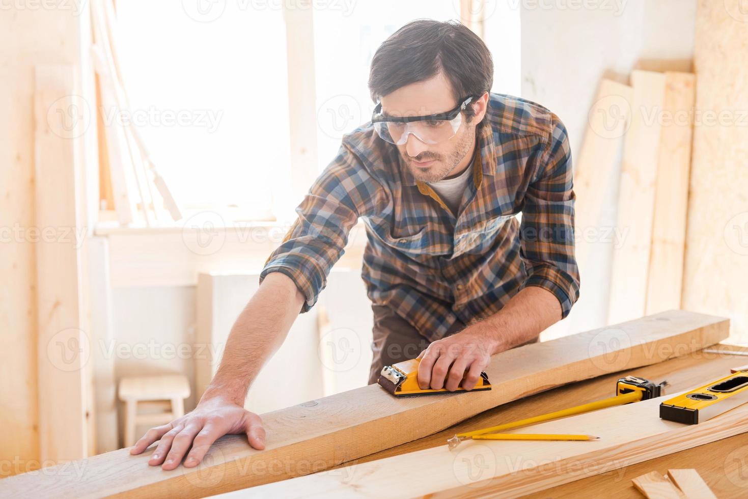 Everything should be perfect. Concentrated young male carpenter in protective eyewear working in his workshop photo