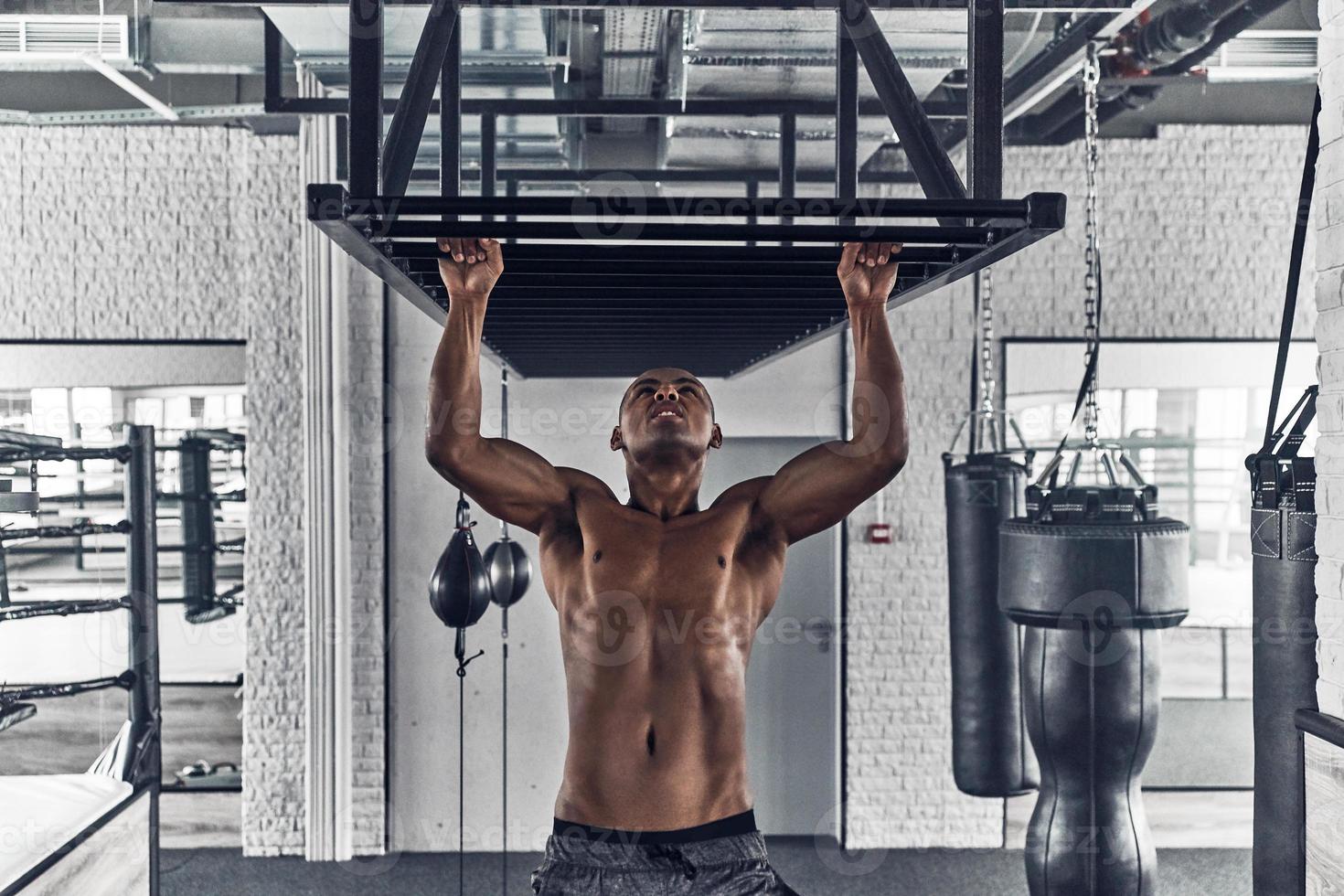 Morning work out. Handsome young African man doing pull-ups while exercising in the gym photo
