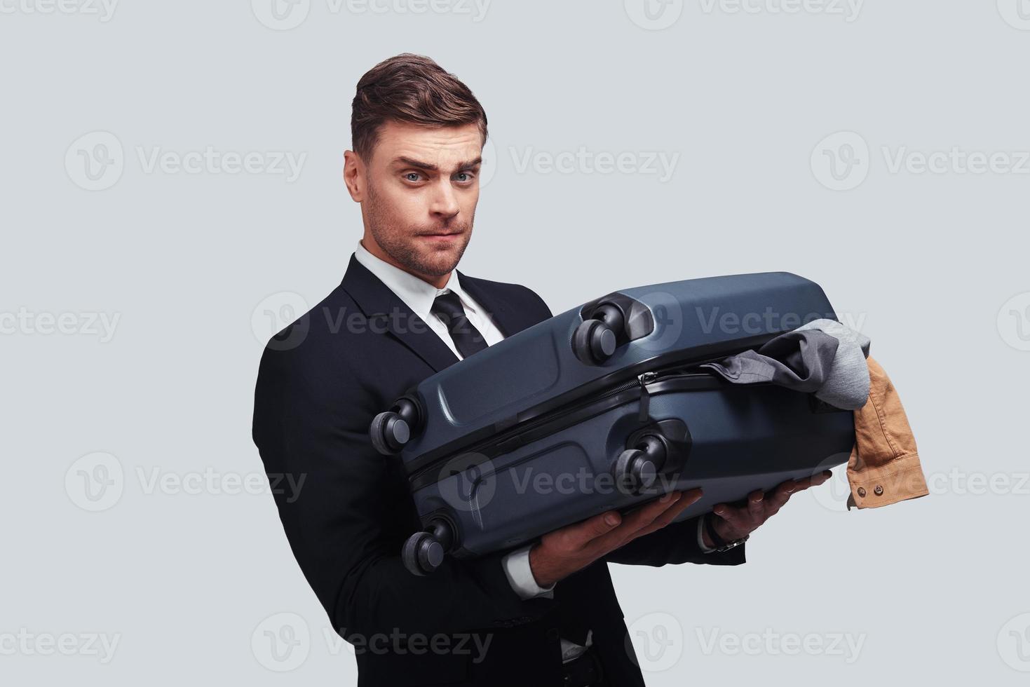 How to deal with this luggage Good looking young man carrying full over packed suitcase while standing against grey background photo