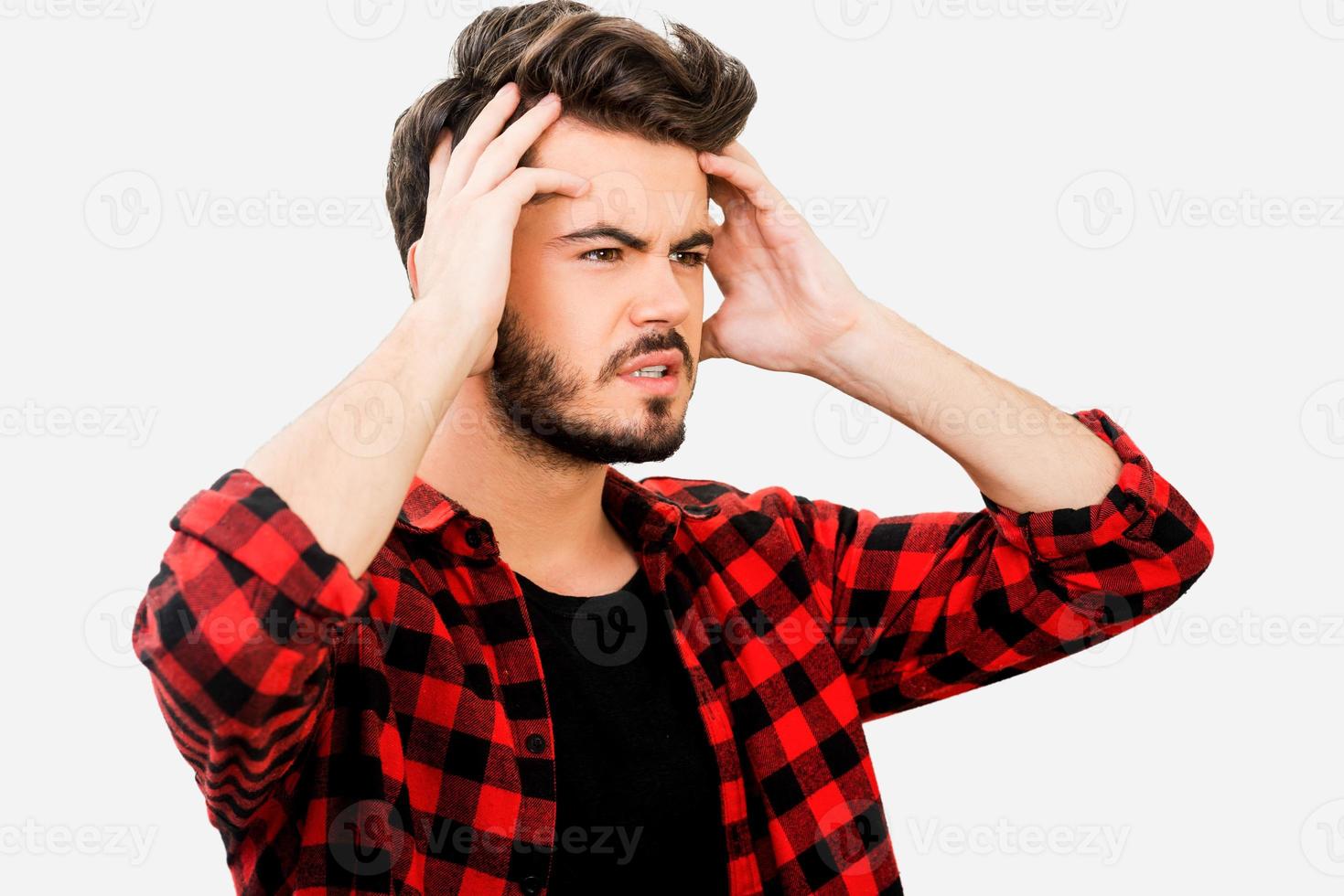 Having some troubles. Frustrated young man holding head in hands and looking away while standing against white background photo