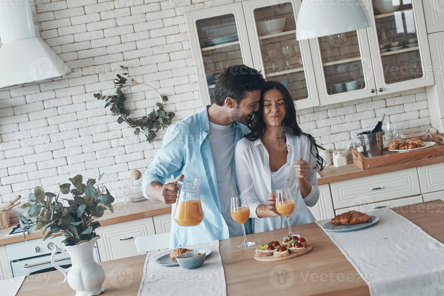 feliz pareja joven preparando el desayuno juntos y sonriendo mientras pasan tiempo en la cocina doméstica foto