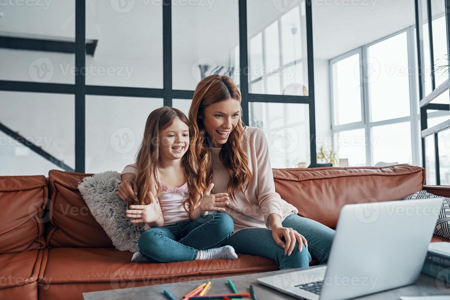Young beautiful mother and her little daughter bonding together and smiling while using laptop at home photo