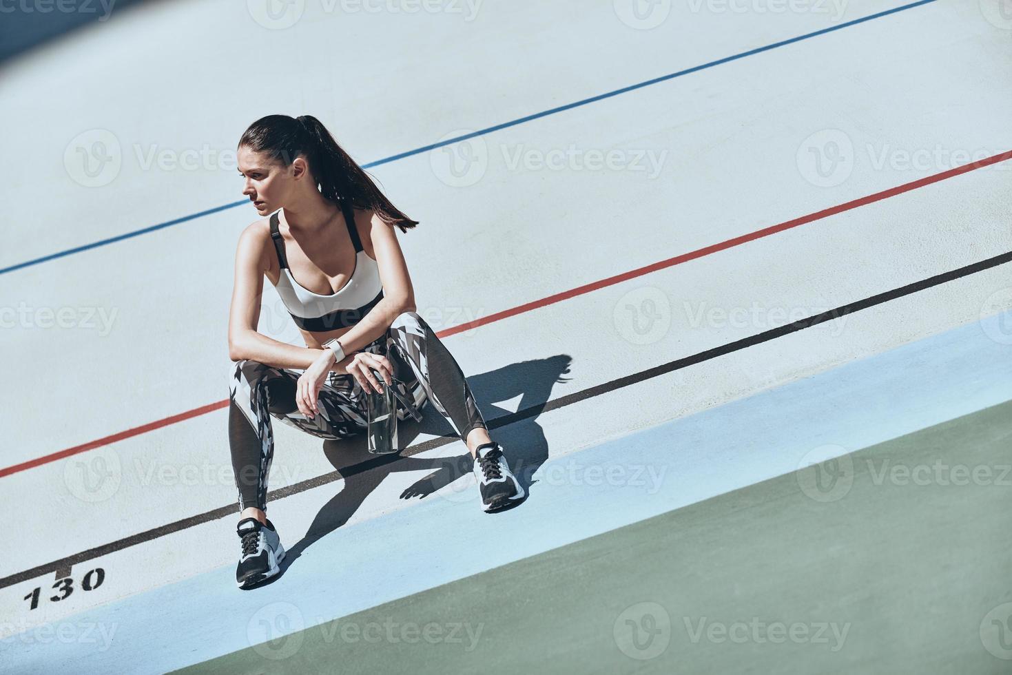 Time to relax. Top view of young woman in sports clothing looking away while sitting on the running track outdoors photo