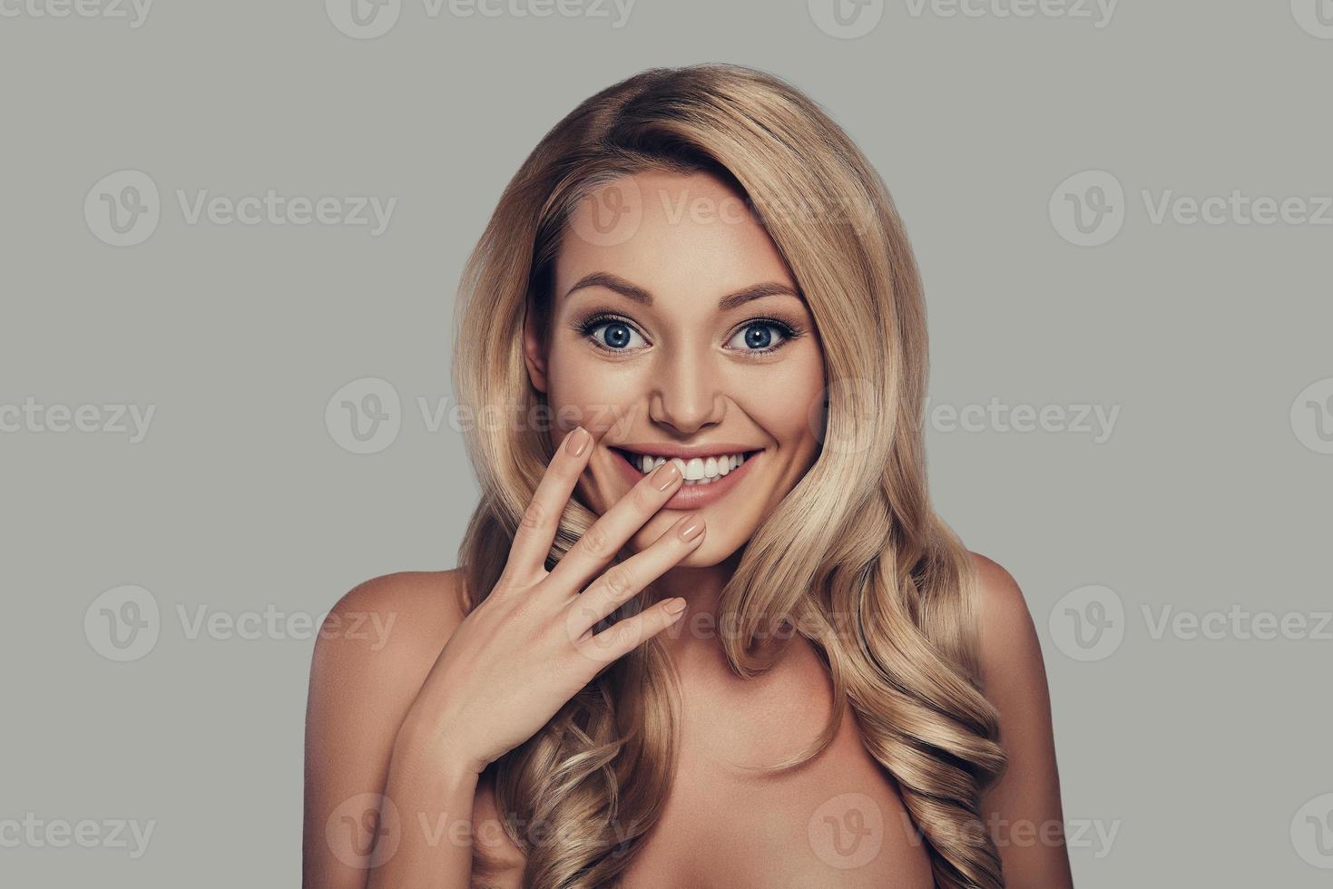 Playful beauty. Beautiful young woman smiling and looking at camera while standing against grey background photo