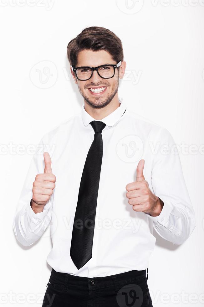 Used to success. Confident young man showing his thumbs up and smiling while standing against white background photo