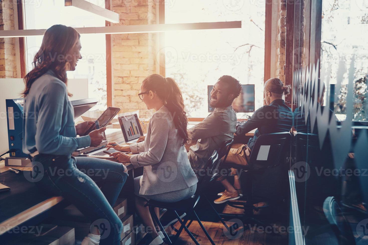 Group of young modern people in smart casual wear communicating and using modern technologies while working in the office photo