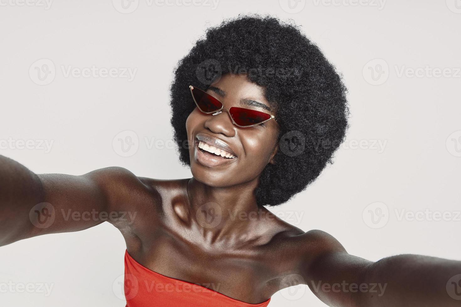 Beautiful young African woman making selfie while standing against gray background photo