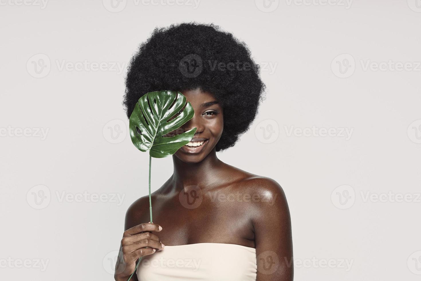 Portrait of beautiful young African woman holding plant near face and smiling photo