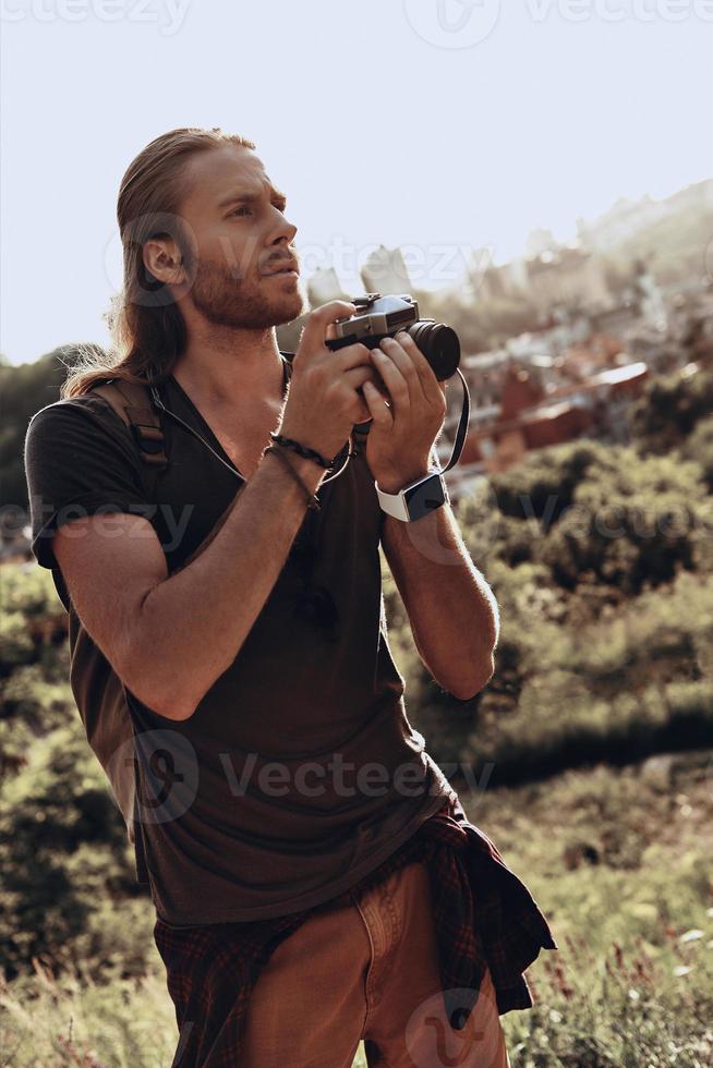 explorando el nuevo lugar. joven con ropa informal fotografiando la vista mientras está de pie en la colina al aire libre foto