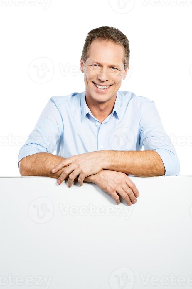 Advertising your product. Happy mature man leaning at the copy space while standing against white background photo