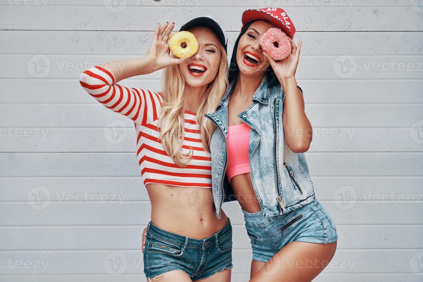 Sweetie beauties. Two playful young women holding donuts against their eyes and smiling while standing against the garage door photo