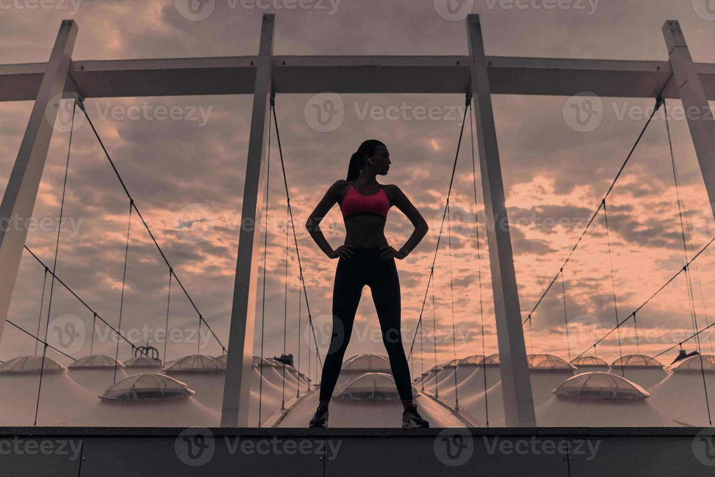 Feeling the freedom. Full length of modern young woman in sports clothing keeping hands on hips and looking away while standing outdoors photo