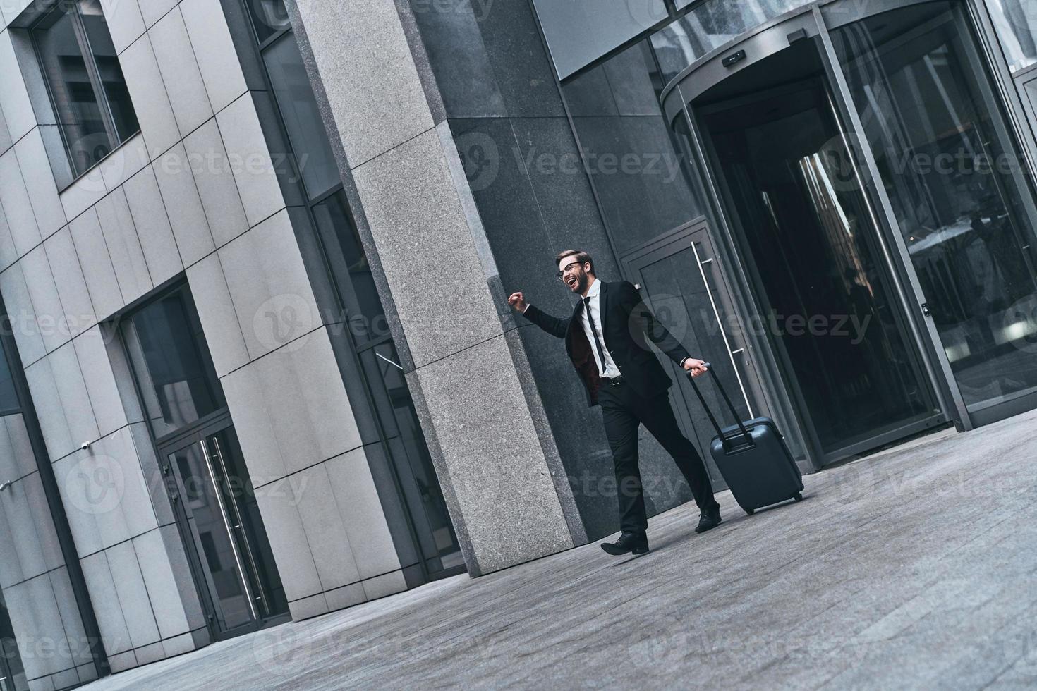 apuesto joven hombre de negocios con traje completo sonriendo y sosteniendo un documento mientras camina al aire libre foto