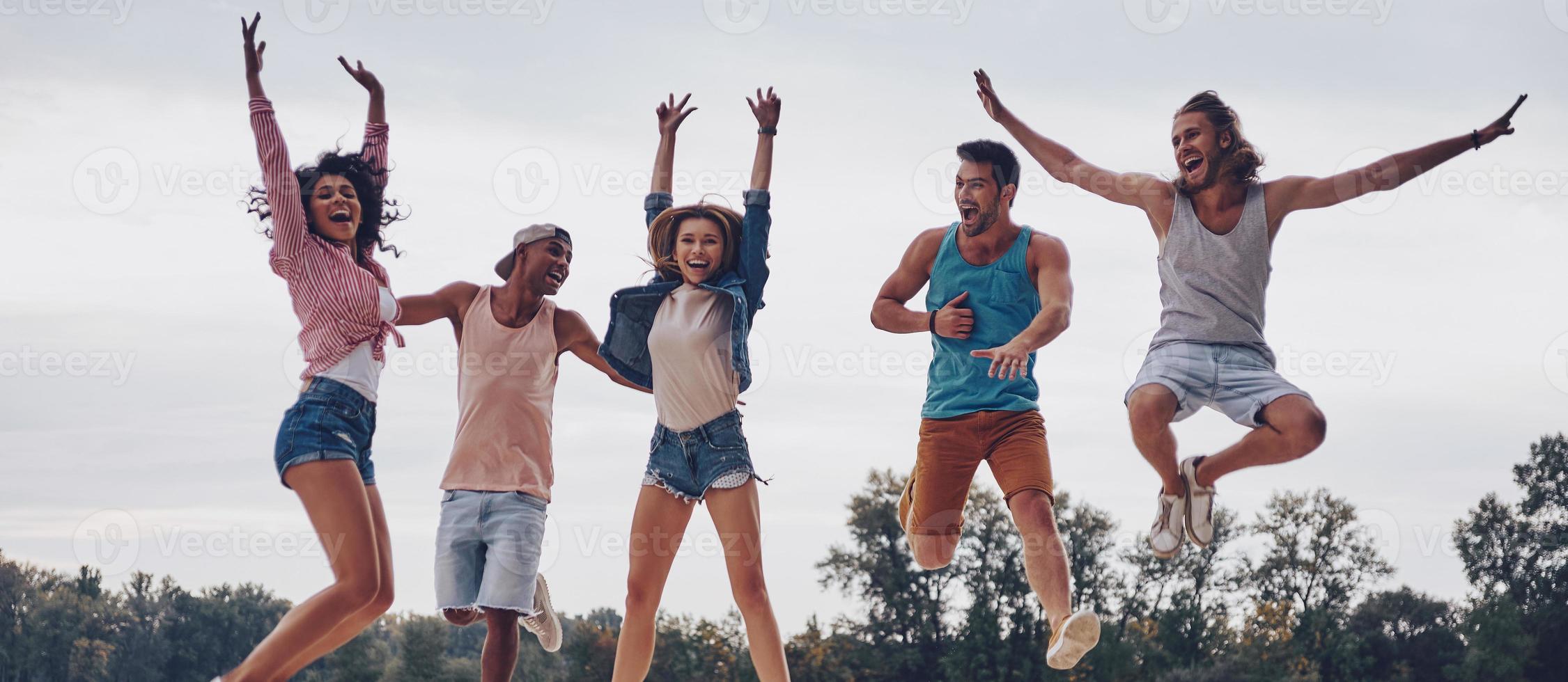 disfrutando de su libertad. toda la longitud de los jóvenes con ropa informal sonriendo y gesticulando mientras saltan en el muelle foto