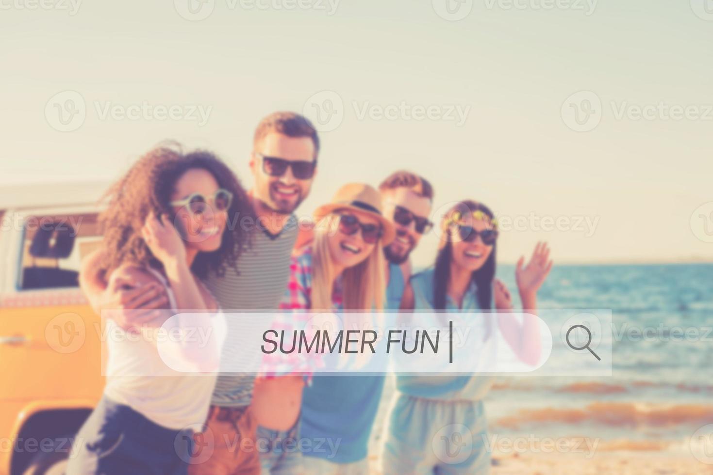 Summer fun. Group of cheerful young people embracing and looking at camera while walking along the beach photo
