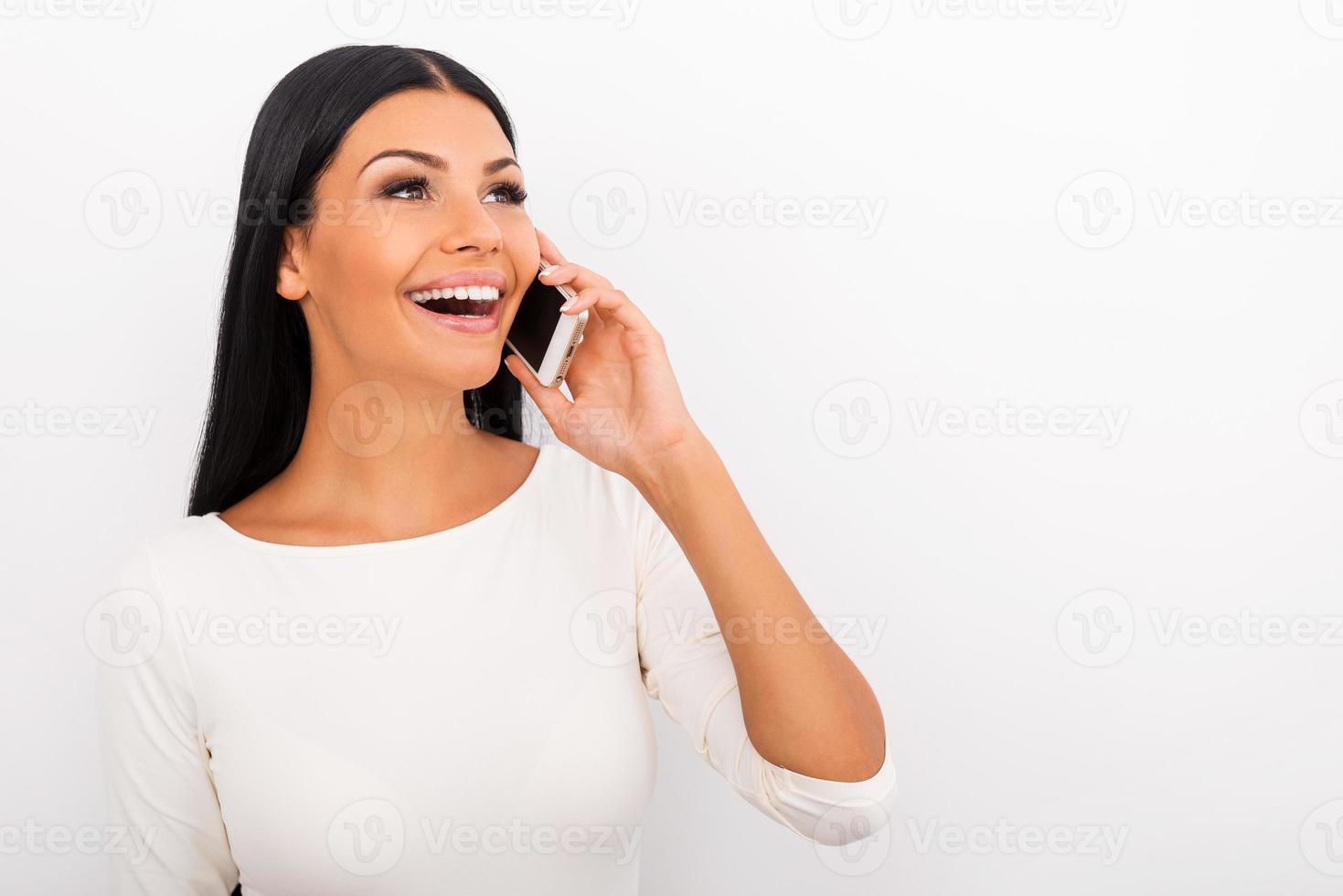 Nice talk with lovely person. Happy young woman talking on the mobile phone and looking away while standing against white background photo