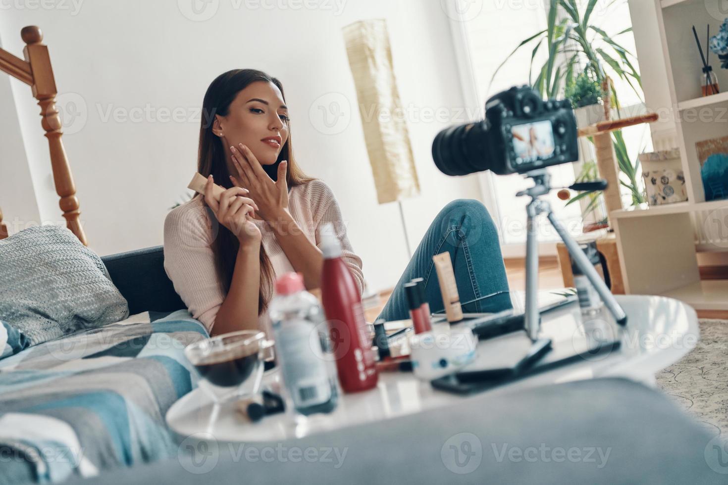 Beautiful young woman applying beauty product and smiling while making social media video photo