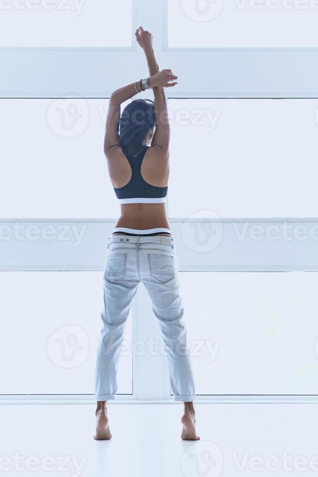 Feeling free and confident. Full length rear view of beautiful young woman keeping hands raised while standing near the window photo