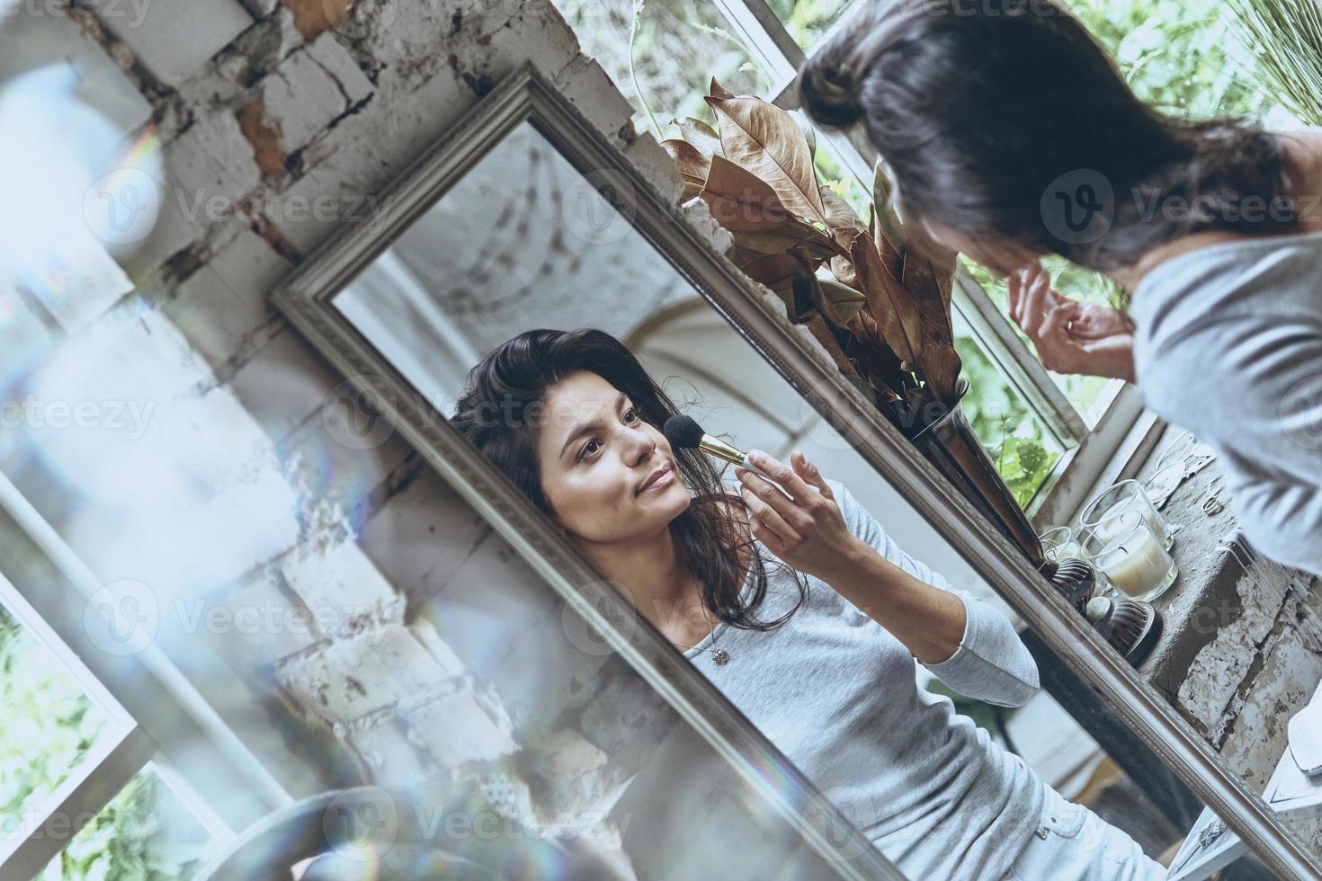 She looks just perfect.  Attractive young woman putting on some make-up while spending time at home photo