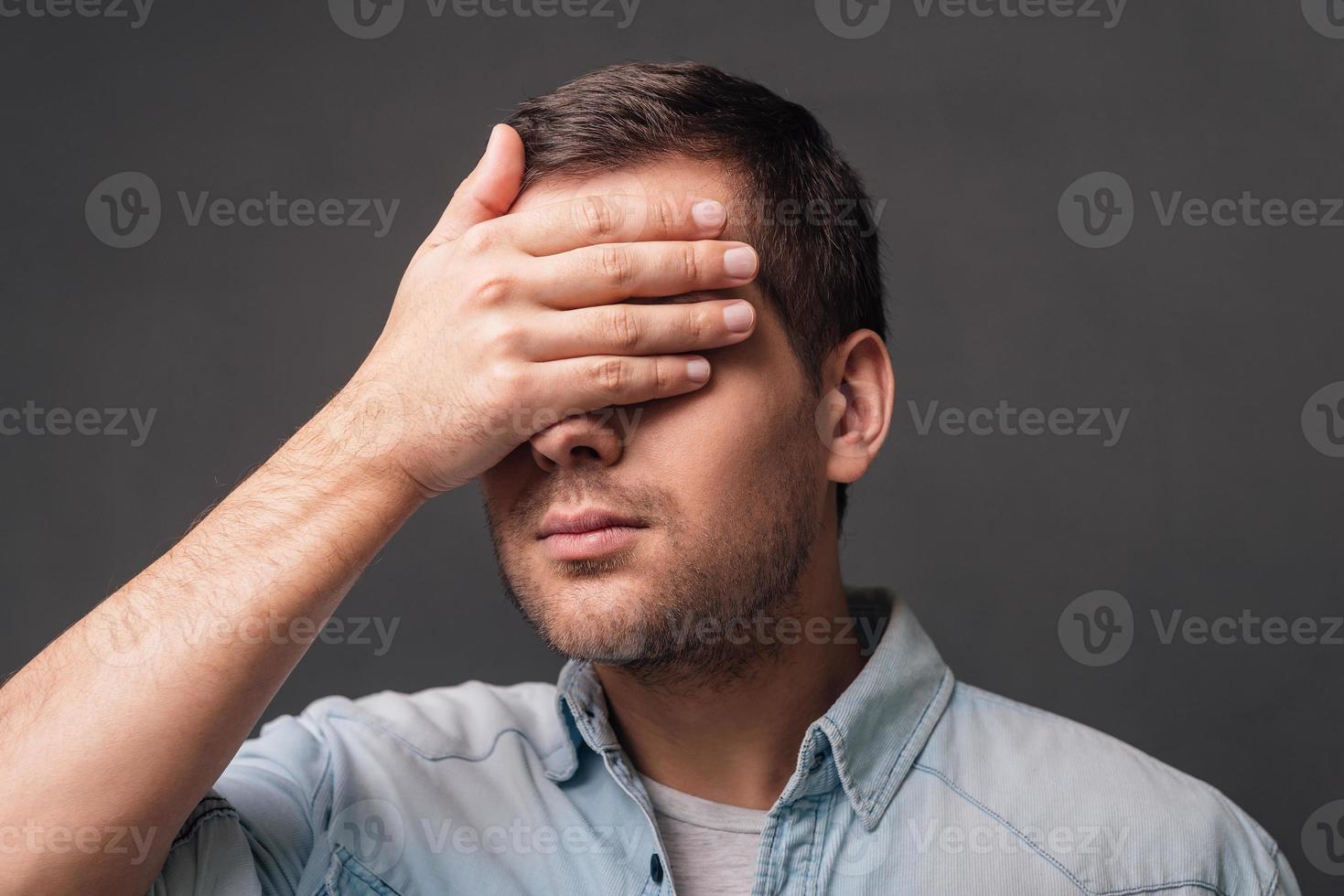 Hide and seek Young handsome man covering his eyes with his hand while standing against grey background photo