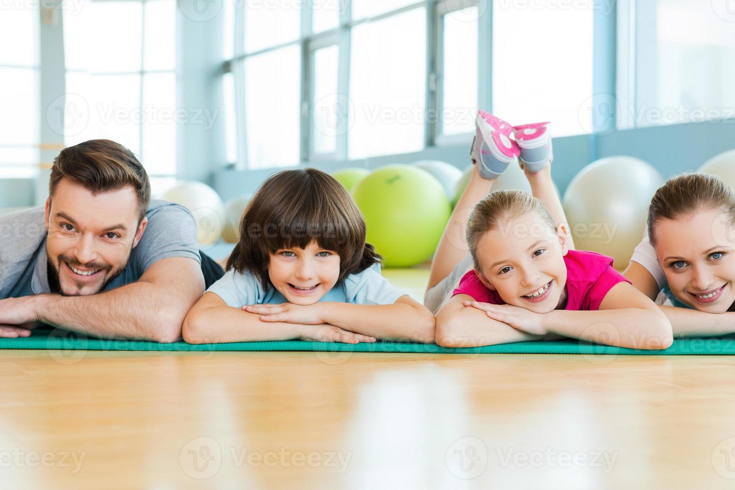 feliz familia deportiva. familia feliz uniéndose entre sí mientras están acostados en la alfombra de ejercicio en el club deportivo foto