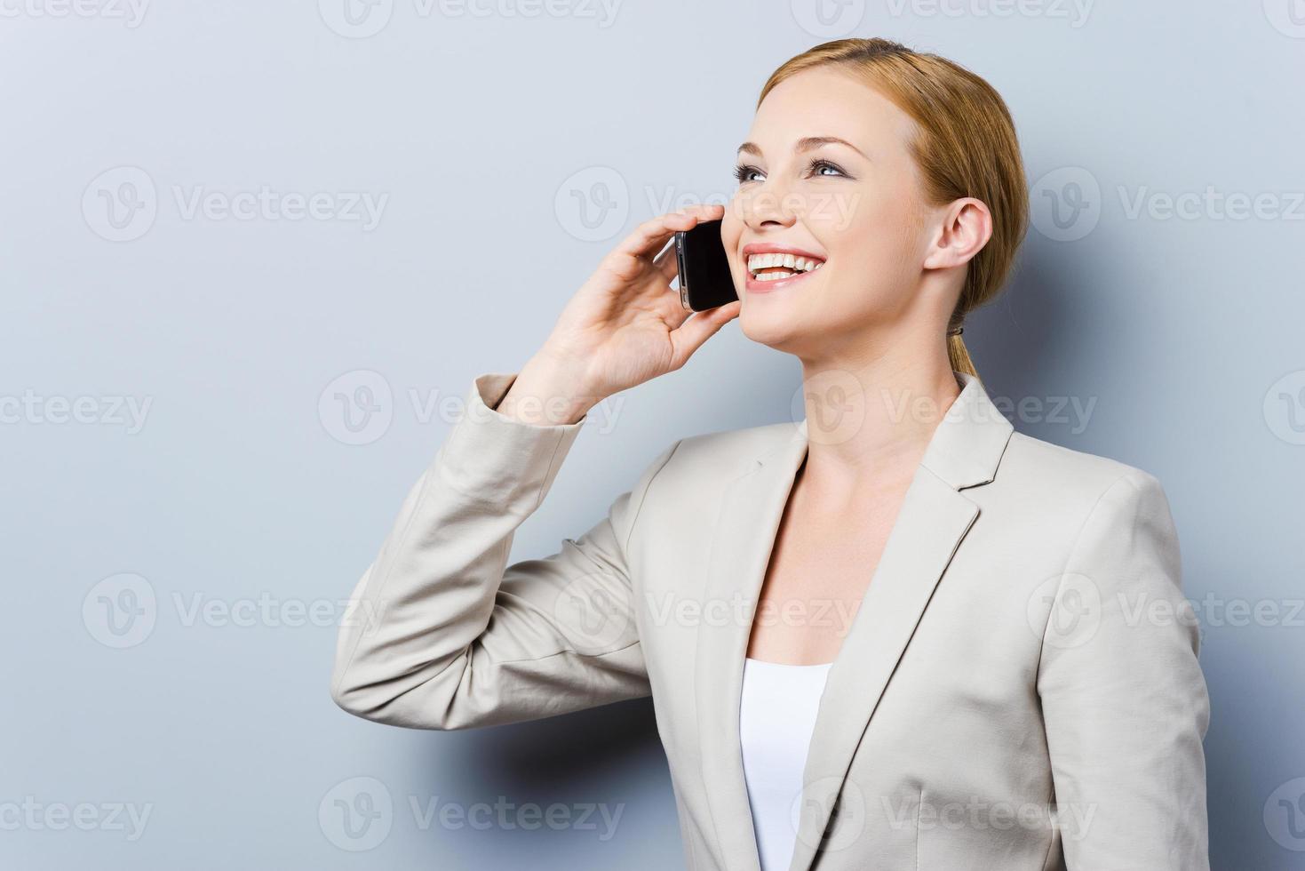 Conversation with pleasure. Beautiful young businesswomen talking on the mobile phone and smiling while standing against grey background photo