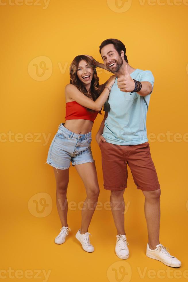 Full length of beautiful young couple smiling while standing against yellow background photo
